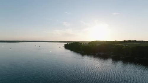 aerial drone shot of lake with boats and the sun peaking over the forest horizon