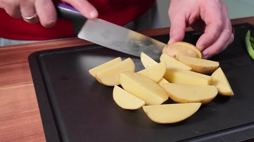 Plan rapproché de mains coupant une pomme de terre fraîche en morceaux égaux sur une planche à découper avec un couteau tranchant