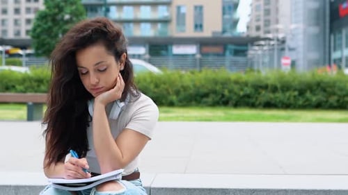 Close Up of Pretty Young Woman Writing in Notebook Outdoors
