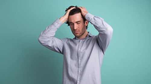 Frustrated Man Suffering From Headache in Blue Studio