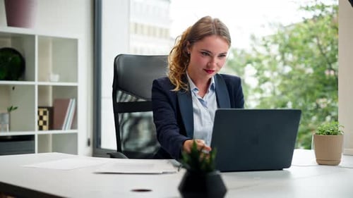 in a Modern Office with a Large Window a Beautiful Worker in a Blue Shirt with a Laptop Looks at the