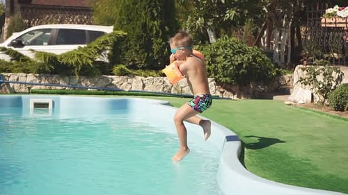Cute Boy in Swimming Trunks Armbands and Water Glasses Jumps Into the Pool on a Sunny Day