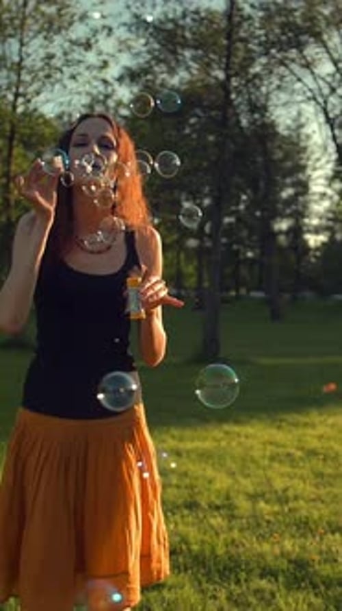Vertical of Beautiful Young Redhair Girl Blowing Soap Bubbles Outdoors Sunset