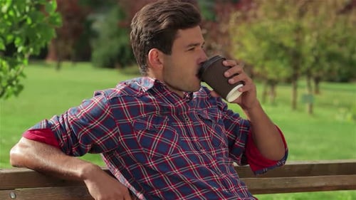 Young Man Enjoying Coffee on a Park Bench
