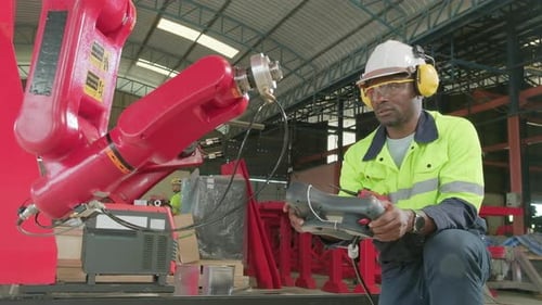 Black engineer test and control robotic arm in mechanical manufacturing factory.