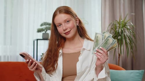 Woman Checks Phone While Holding Money