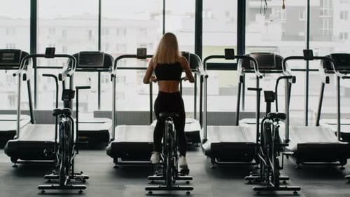 Woman Exercising on Bike in Bright Gym