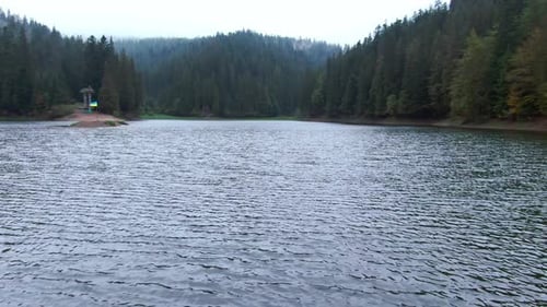 Drone Flying Over Blue Deep Lake Synevyr to Evergreen Forest in Carpathian Mountains Wide Shot Water