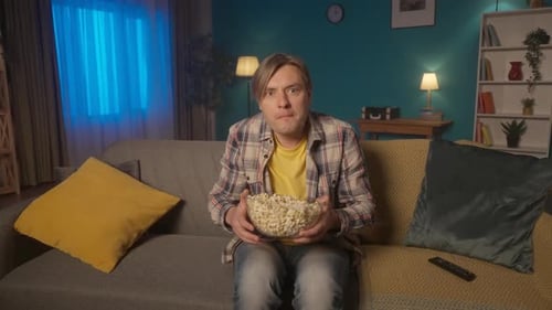 Shocked Man Watching a Scary Movie on TV at Home and Eating Popcorn The Man Shudders in Fear and