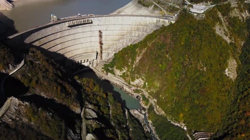 Riesiger Wall of View Dam aus Beton inmitten majestätischer Berge, die von grünem Wald bedeckt sind