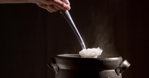 The cook is cooking rice porridge in a boiling clay pot with steam coming out