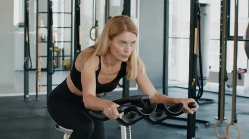 Motivated Woman Athlete Exercising on Bicycle Training Apparatus at Gym Preparing for Bike Marathon
