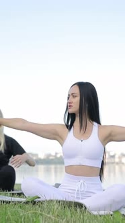 Vertical Video European Young Women are Doing Yoga While Sitting on the Shore of the Lake