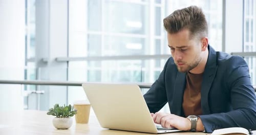 4k video footage of a handsome young businessman working on his laptop in the office