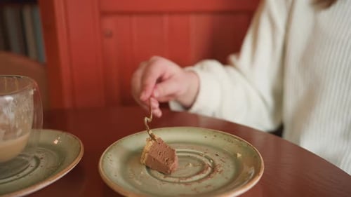 Close Up of Hand Slicing Chocolate Cake Beside Latte on Round Table