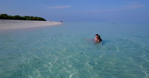 Happy couple swim on clear crystal water of shallow lagoon near white beach of tropical island under