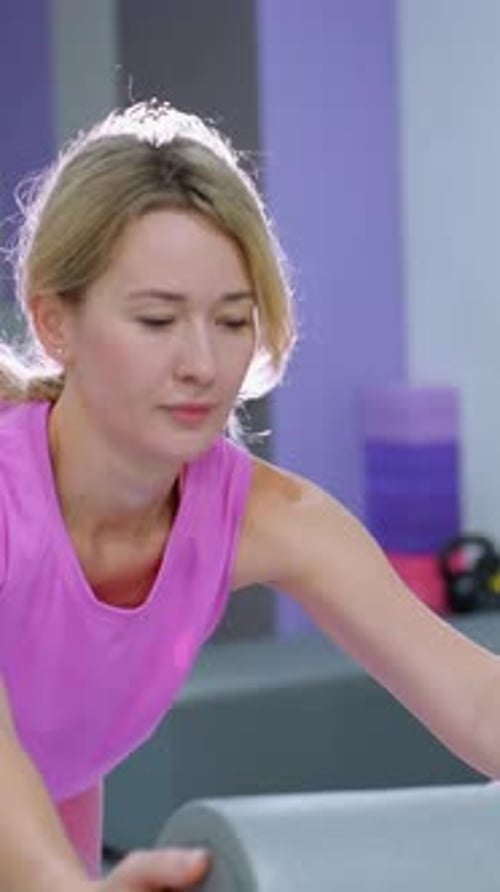 Femme s'étirant avec un rouleau en mousse dans une salle de sport bien éclairée