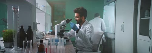 Scientist Analyzing Sample Under Microscope in Bright Lab