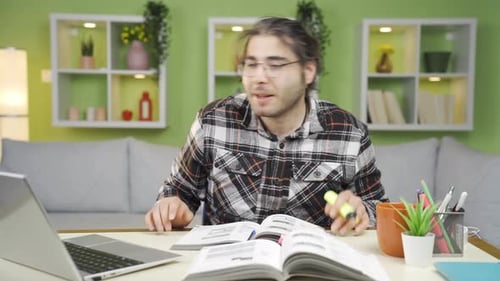 Young Adult Studying at Home with Laptop and Book
