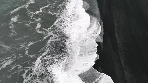 White foamy waves arrive to the beach with black sand in Iceland.