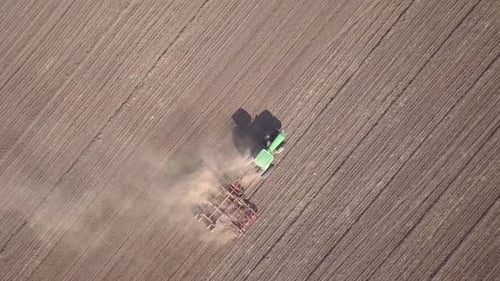 Top Down Aerial View of Green Tractor Cultivating Ground and Seeding a Dry Field Farmer Preparing