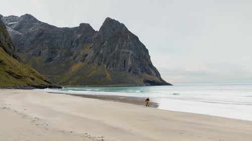 One man running on Kvalvika beach in Lofoten islands below large cliffs