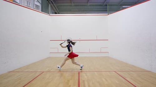 Athletic Woman Hits Ball Against Front Wall on Squash Court