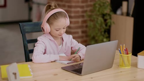 Blonde Girl Writes in Notebook Wearing Pink Headphones