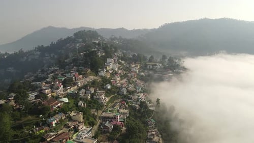 Aerial shot of a city in the mountains covered with clouds in the morning.