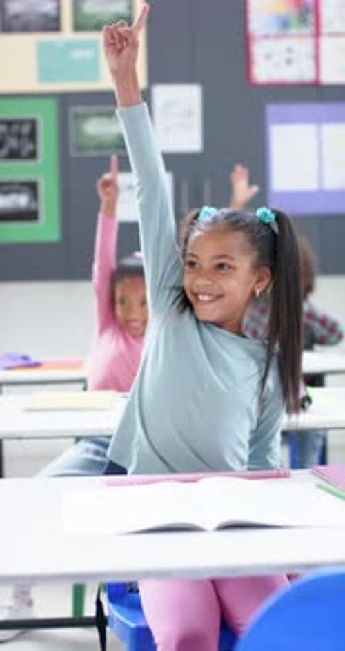 Vertical video: In school, girl raising hand in classroom, actively participating in lesson