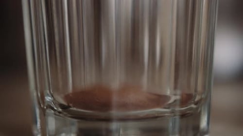 Instant powdered coffee scooped into transparent glass, shallow focus close-up, slowmo