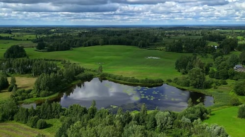 Aerial Timelapase reflected clouds pass over a lake green fields of a rural town