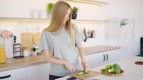 Woman Smiling, Cuts Cucumber in Bright Kitchen