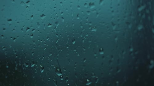 Rain water drops falling down on the blue window glass. Close up