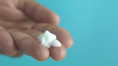 Hand Holding White Lotion on Blue Background
