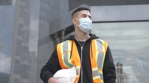 Hispanic construction worker stands confidently in face mask on building site