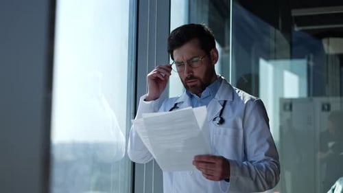 Tired Doctor Reviews Documents in Hospital Setting