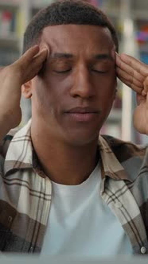 Stressed African American Man Student in Library Massaging Head Headache Eyes Closed Migraine Guy