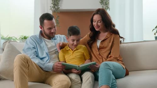 Happy Caucasian Family Dad Mom Son Reading Fairytale Story Book on Sofa in Cozy Living Room Caring