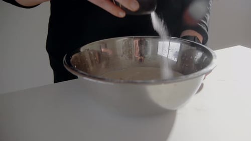 Junge Frau schnurrt Salz in eine Schüssel mit Milch und macht zu Hause Teig für einen Kuchen in der Küche. Homema