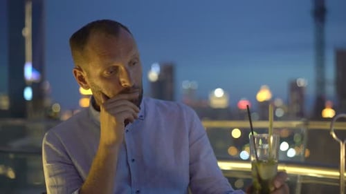 Sad, Unhappy Man Drinking Cocktail Sitting on Terrace in Bar at Night Alcohol
