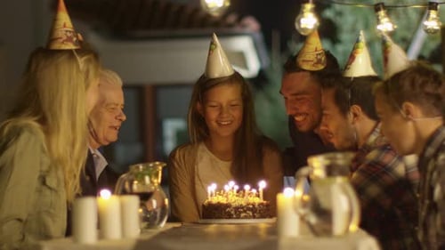 Happy Smiling Girl Blowing Candles out on her Birthday Cake. Girl Surrounded by Her Family and Frie