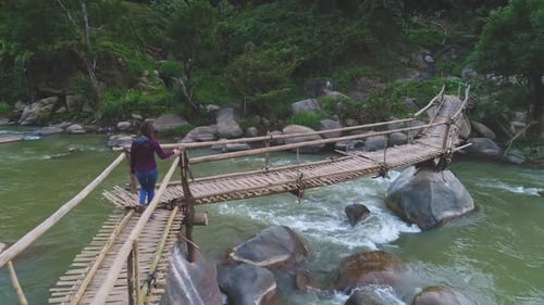 Young Woman Enjoying the View From a Bamboo Bridge Over a River in the Jungle