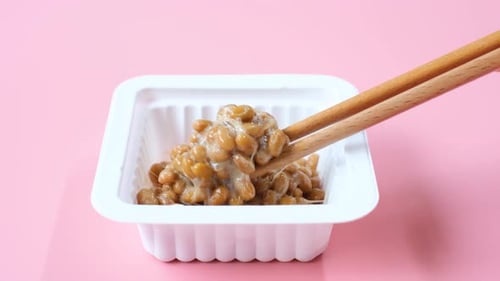 Wooden chopsticks holding Japanese natto beans on pink background top view.