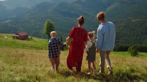 Unrecognizable family coming down green hill enjoying summer vacation in mountains