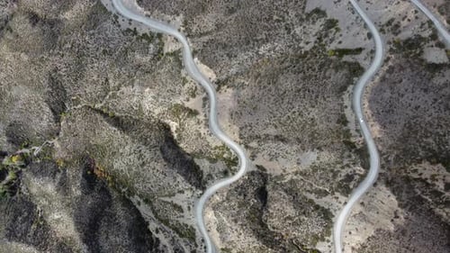Aerial: Lone car climbs arid mountain pass on gravel road switchback