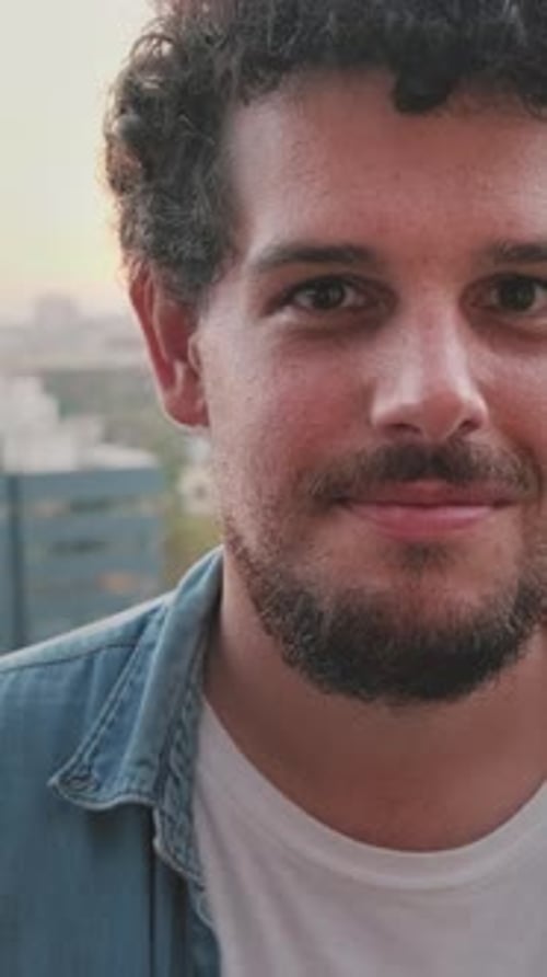 Nahaufnahme eines lächelnden jungen Mannes, der vor der Kamera posiert, während er auf dem Balkon steht