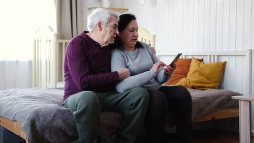 Loving Senior Couple Using Smartphone Together Indoors