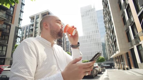 Man Using Smartphone and Drinking Coffee in City