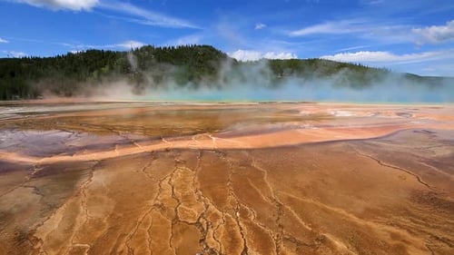 Static view of geothermal geyser and hot spring with blue steam cloud rising and mountains in the ba